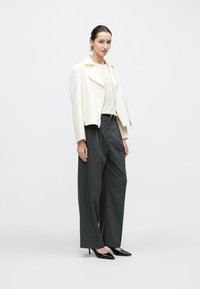 Hvid læder bikerjakke, figursyet i taljen, kombineret med løstsiddende mørkegrå bukser og sorte spidse hæle, minimalistisk design.