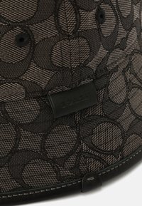 Cappello a secchiello nero realizzato in tessuto texturizzato con motivi circolari, un'etichetta in pelle e cuciture a contrasto lungo il bordo.