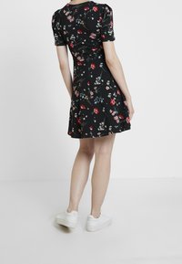 Černé květinové šaty s nafouknutými rukávy, zdobené barevným květinovým tiskem a rozšířenou sukní. Spárováno s bílými teniskami.