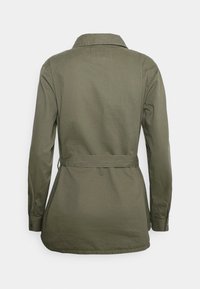 Giacca verde oliva a maniche lunghe con colletto, vita con cintura e taglio dritto. Tessuto liscio senza modelli o accenti visibili.