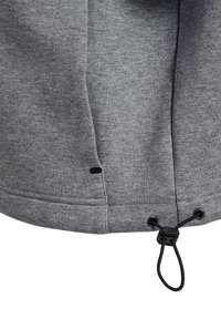 Tessuto di felpa grigia con una texture liscia, dotato di un cordoncino all'orlo, una cucitura rinforzata e un piccolo accento a forma di buco nero.