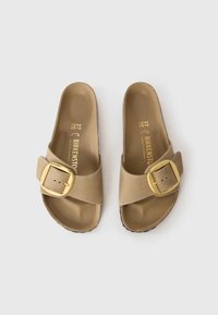 Svetlo rjave Birkenstock sandale s širokim trakem, zlatim sponko in oblikovanim podplatom. Gladka tekstura z obliko za enostavno natikanje. Velikost 37.