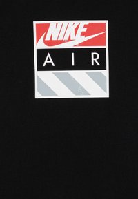 Melna auduma, kas izceļas ar ievērojamu taisnstūrveida Nike logo sarkans un balts, ar vārdu "AIR" biezām balta burtiem un pelēkiem diagonāliem svītrām.