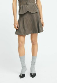 Gewellter brauner Rock mit Nadelstreifen, flared Schnitt, tailliertem Bund und einem Peplum-Akzent, kombiniert mit gerippten grauen Socken und schwarzen spitzen Schuhen.