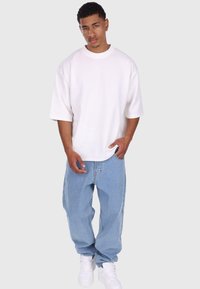 Overdimensioneret hvid t-shirt med korte ærmer, kombineret med løse, lyseblå denimjeans og hvide sneakers. Enkel design uden mønstre eller accenter.