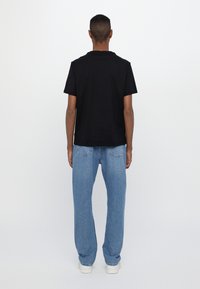 Camiseta de algodón negra de manga corta combinada con jeans de mezclilla azul claro, con pierna recta y un ajuste relajado. Se ven zapatillas blancas.