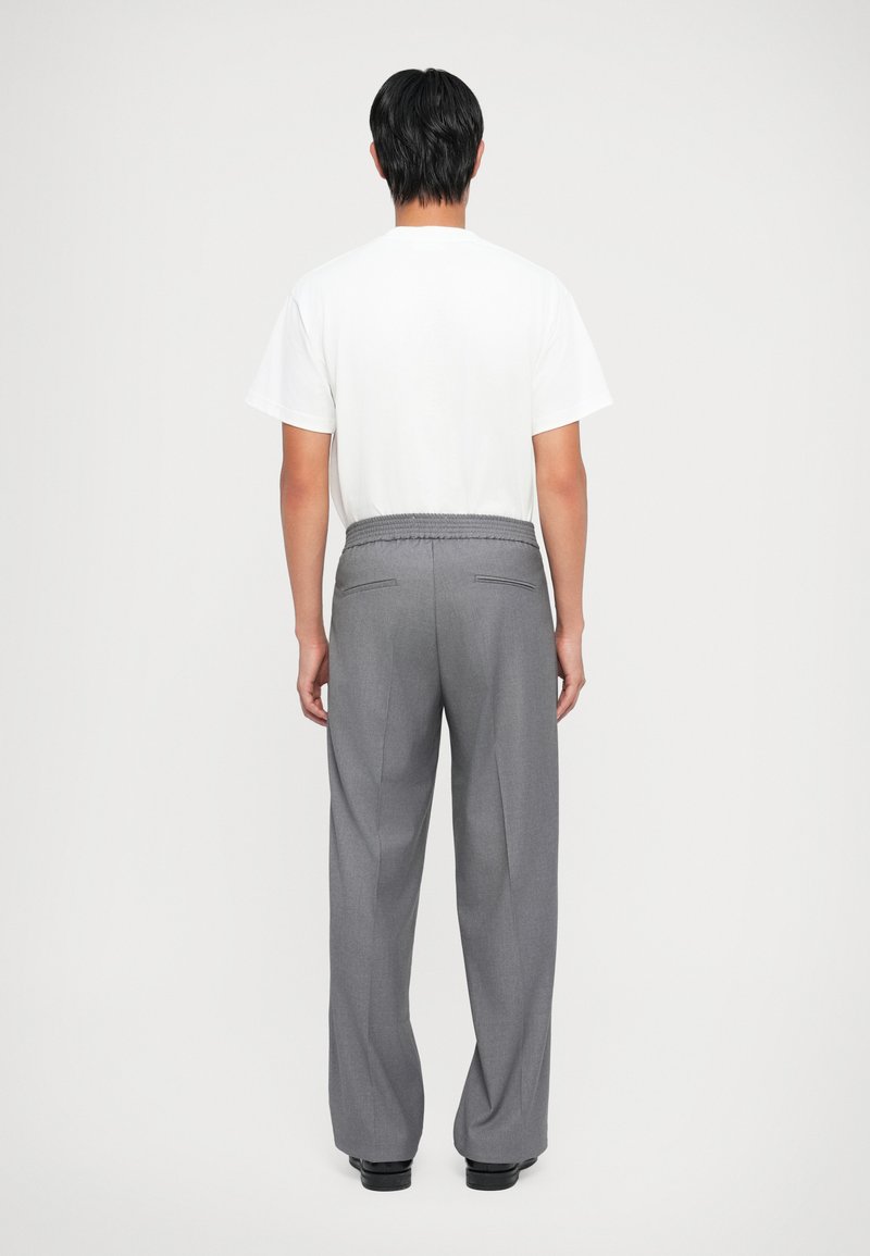 Pantalons gris ajustés avec une coupe décontractée, taille élastique et poches arrière. Associés à un T-shirt blanc uni.