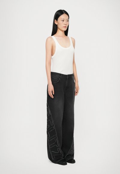 Black wide-leg jeans with side embroidery, paired with a white tank top. Features a high waist and five pockets. Smooth denim texture.