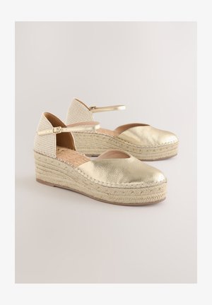 Kuldse metallilise viimistlusega kiilkontsaga sandaalid avatud varbaga, punutud jutigaaniga tald ja mustrilise kangaga tagakülg. Põlveümbruse rihm pandlaga detailiga.