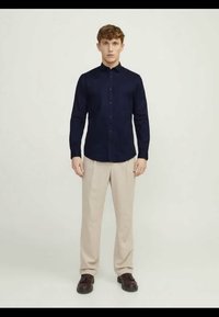 Tummansininen nappipaita pitkillä hihoilla, yhdistettynä vaaleisiin housuihin. Paidassa on klassinen kaulus ja slim fit -leikkaus, ja se on valmistettu pehmeästä kankaasta.