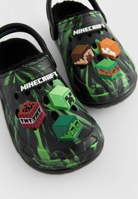 Fekete klumpák zöld grafikai dizájnnal, bolyhos béléssel és három Minecraft témájú charm-mal a tetején: TNT, Steve és egy creeper.