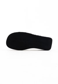 Czarna gumowa podeszwa buta o prążkowanej fakturze. Lekko zakrzywiony kształt i płaski design. Z gładką krawędzią i bez widocznych oznaczeń.