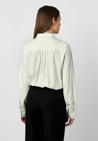 Hellgrünes Langarmhemd mit Kragen und einer Rückenfalte. Kombiniert mit schwarzen maßgeschneiderten Hosen. Glatte Textur, minimalistisches Design.