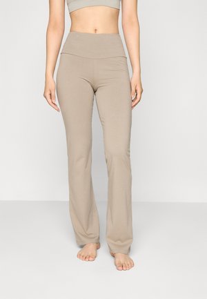 Leggings beiges longs avec une taille haute, fabriqués en matière stretch douce, présentant une texture lisse et un design minimal.