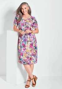 Blumenkleid in Rosa-, Lila- und Gelbtönen mit kurzen Ärmeln und rundem Ausschnitt, kombiniert mit braunen Keilsandalen.