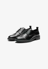 Chaussures en cuir noir avec une finition lisse. Présentent un laçage à l'avant, une pointe arrondie et un petit talon. Accents en textile sur le dessus.