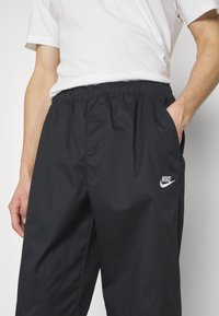 Svarta Nike-byxor med elastiskt midjeband, sidofickor och en vit logotyp. Slätt, lätt material med lös passform.