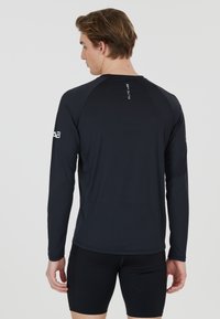 Langarm sportshirt in donker marineblauw, met een aansluitend ontwerp, een soepele textuur en subtiele logo-details op de mouwen en de rug.