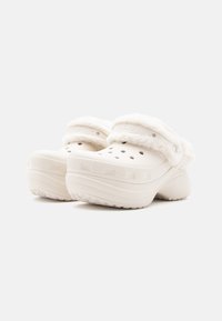 Fehér Crocs szandál puha, műszőrme bélésű mandzsettával, szellőzőnyílásokkal és tapadós, texturált talppal. Lekerekített formájú, emelt sarokkal.