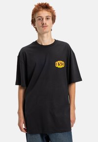 Zwarte katoenen T-shirt met korte mouwen en eenRelaxte pasvorm, met een gele "OSCO" logo op de linkerborst.