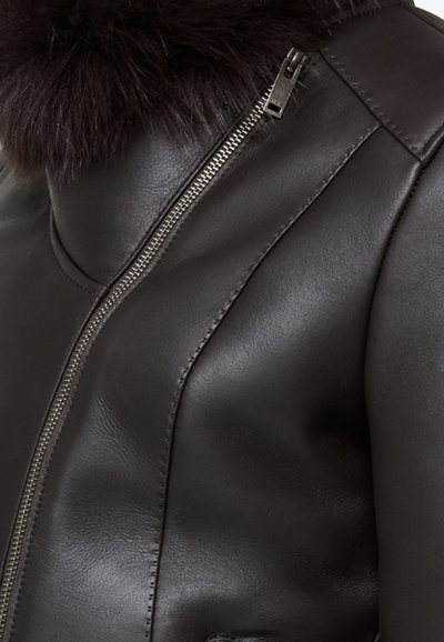 Giubbotto in pelle marrone scuro con chiusura lampo argentata e dettagli di pelo scuro, mostrato in primo piano.