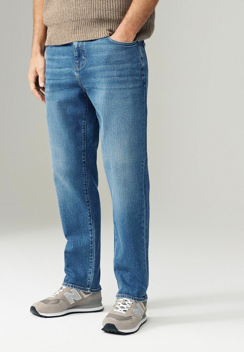 Jeans in denim blu chiaro con taglio dritto, tasche anteriori e una finitura leggermente sbiadita, abbinati a sneakers grigie.