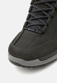 Svart semsket og tekstil fotturssko med snøring, gummisåle og GORE-TEX-merke, med søm detaljer og en teksturert overflate.