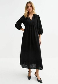 Robe maxi noire avec un décolleté en V, des manches bouffantes trois-quarts avec des détails brodés, et une taille froncée. Tissu léger avec une finition texturée.