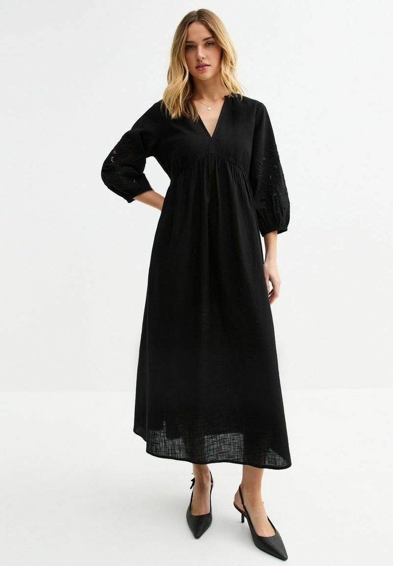 Robe maxi noire avec un décolleté en V, des manches bouffantes trois-quarts avec des détails brodés, et une taille froncée. Tissu léger avec une finition texturée.