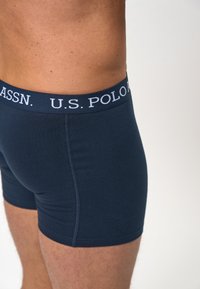 Sötétkék boxer alsónadrág elasztikus anyagból, puha derékrésszel, amelyen fehér betűkkel szerepel a "U.S. POLO ASSN.", testhezálló fazon.