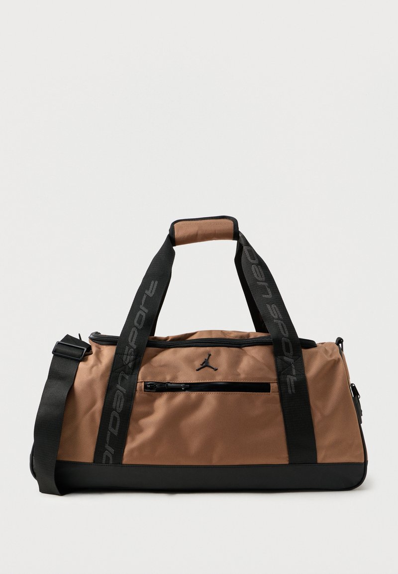 Mala de desporto em nylon castanho com detalhes pretos, apresentando alças superiores, uma alça de ombro removível e um bolso frontal com fecho. Logotipo da Jordan exibido.