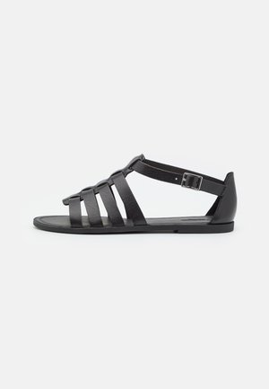 Schwarze Ledersandalen mit mehreren horizontalen Riemen, einem Knöchelriemen mit Schnalle und flacher Sohle. Minimalistisches Design mit glatter Textur.