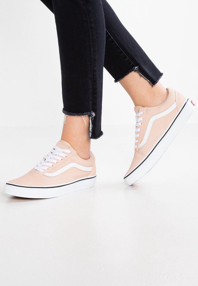 Ljust rosa canvas sneakers med vita snören, svarta och vita detaljer samt en texturerad yta. Bärs tillsammans med mörka jeans med fransade fållar.