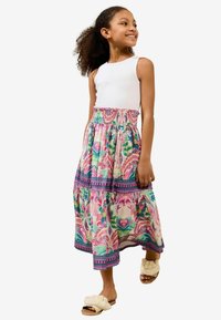 Rochie maxi cu top fără mâneci alb și fustă cu un model floral colorat; prezintă un tiv volanat și o talie elastică. Asortată cu sandale pufoase de culoare bej.