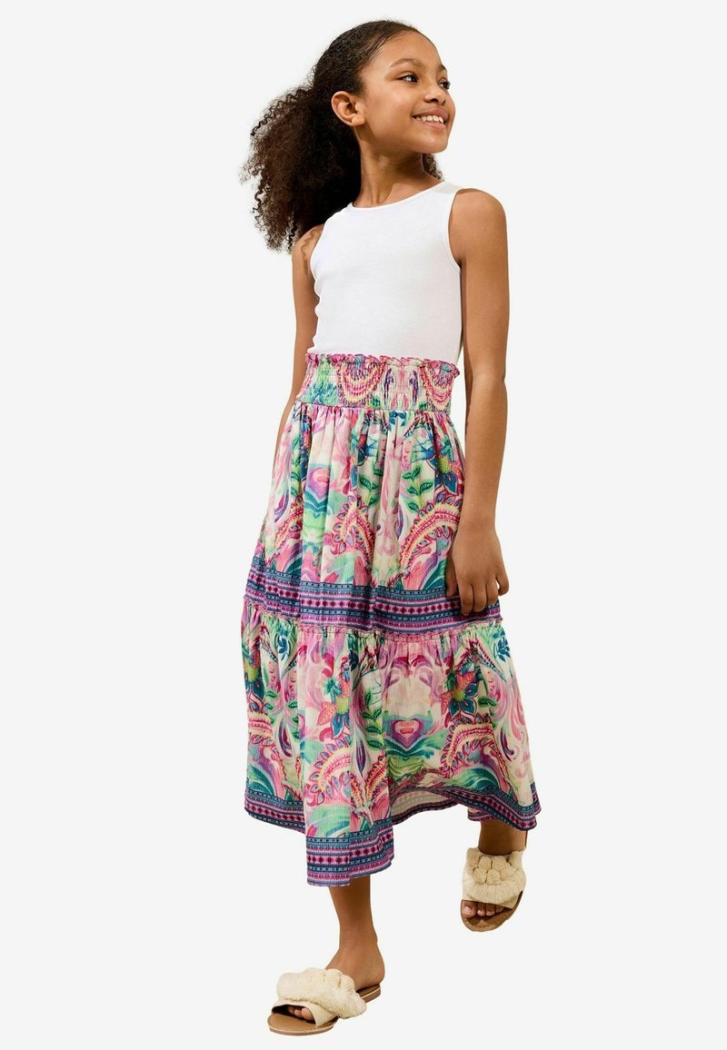 Rochie maxi cu top fără mâneci alb și fustă cu un model floral colorat; prezintă un tiv volanat și o talie elastică. Asortată cu sandale pufoase de culoare bej.