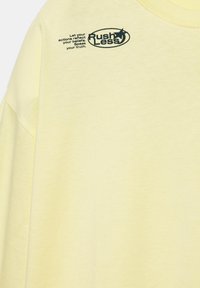 Světle žluté tričko s černým textem a hvězdou u límce s nápisem „Méně spěchej, nech své činy odrážet tvá přesvědčení. Řekni svou pravdu.“