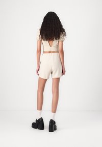 Ensemble beige en deux pièces comprenant un top court avec des manches bouffantes et une découpe dans le dos, associé à des shorts assortis. Chaussures à plateforme noires.