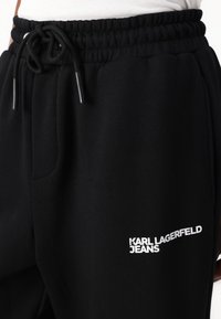Must have kottid mustreid, millel on elastne vöökoht ja reguleeritav pael. Funktsioonide seas on plaastrikott ja valge "KARL LAGERFELD JEANS" logo.