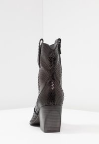Botte de cheville en cuir imprimé serpent noir avec un talon bloc, un bout pointu et des languettes de tirage sur les côtés ; surface texturée avec une finition brillante.