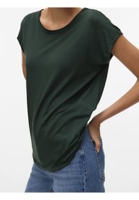 Ciemnozielona koszulka z krótkim rękawem i okrągłym dekoltem, wykonana z lekkiego materiału, luźny fason, z bocznymi rozcięciami, zestawiona z jasnoniebieskimi dżinsami.