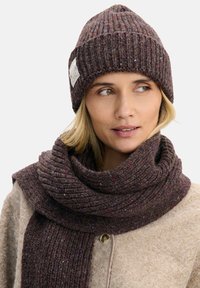 Brązowa prążkowana dzianinowa czapka z daszkiem i pasujący szal z wielokolorowymi plamkami. Szal owija się wokół szyi, ma miękkie, teksturowane wykończenie.