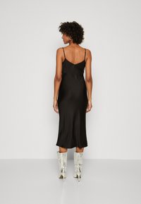 Robe fourreau en satin noir avec des bretelles fines, présentant une coupe mi-longue et une texture lisse et brillante. Assortie à des bottines argentées brillantes.