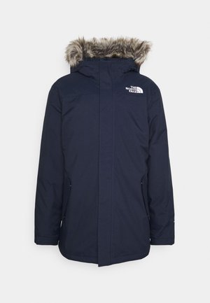 Marineblå North Face vinterparka med hætte med kunstpelskant, lynlås foran og sidelommer, vist mod en ensfarvet baggrund.