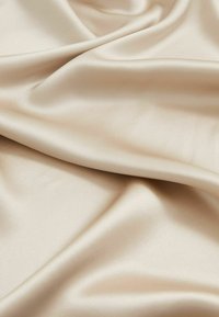 Tejido de satén en un color beige claro, caracterizado por una textura suave, un brillo sutil y un caído fluido con suaves pliegues.