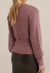 Stickad kofta i dämpad lila färg, med skärp i midjan, ribbad textur och långa ärmar. Kombinerad med en figursydd svart kjol.