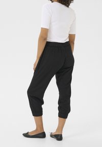 Černé zkrácené kalhoty s elastickým pasem, ribbovanými manžetami a uvolněným střihem, v kombinaci s černými balerínami a bílým přiléhavým topem.