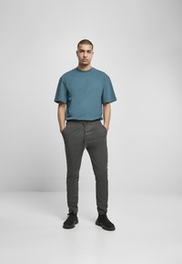 Camiseta de gran tamaño en color verde azulado, joggers gris ajustados con cintura elástica y zapatillas negras. Diseño simple, textura suave y corte casual.