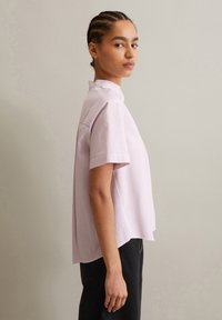 Korte mouwen shirt in lichtroze met witte verticale strepen, met een hoge kraag en een ontspannen pasvorm. Zachte stof met een gladde textuur.