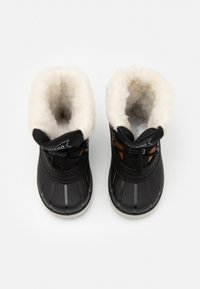 Bottes noires imperméables avec une doublure en fausse fourrure blanche douce, une semelle en caoutchouc texturée et des lacets noirs, avec un accent orange sur le côté.