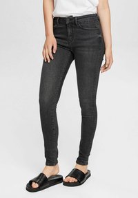 Jeans skinny negros de denim, con una cintura de altura media, diseño de cinco bolsillos y un acabado suave. Combinados con sandalias de plataforma negras.